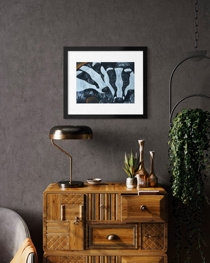 Black framed A3 badger art print on a dark charcoal plaster wall above a walnut art deco chest with a brass dome lamp and trailing ivy.