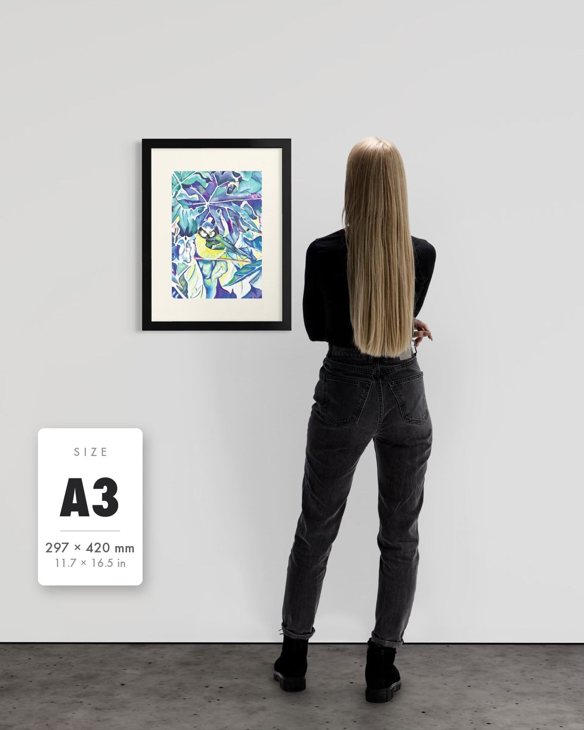 Andrea Nicole 'Taking Flight' blue tit art print in a black A3 frame shown to scale beside a standing woman on a gallery wall, with an A3 (297 × 420 mm) size label. | an:family=print;role=sizeref;size=A3;finish=black