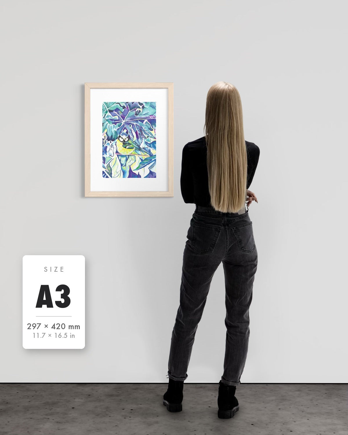 Andrea Nicole 'Taking Flight' blue tit art print in a natural wood A3 frame shown to scale beside a standing woman on a gallery wall, with an A3 (297 × 420 mm) size label. | an:family=print;role=sizeref;size=A3;finish=natural