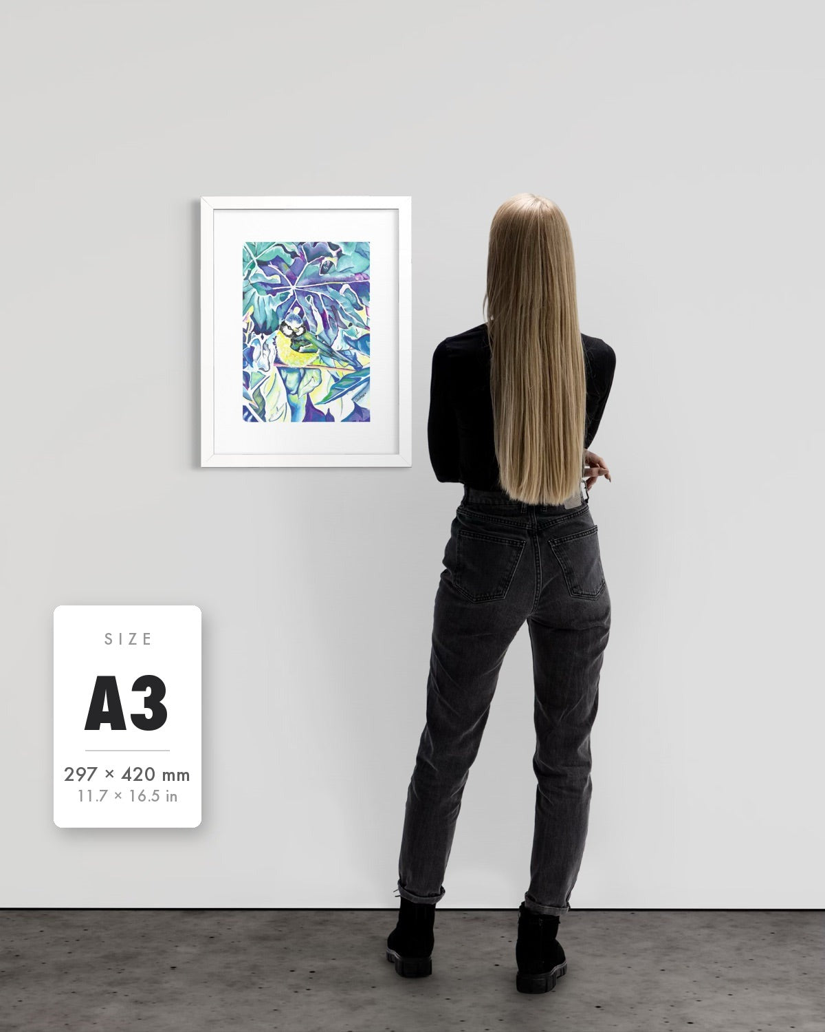 Andrea Nicole 'Taking Flight' blue tit art print in a white A3 frame shown to scale beside a standing woman on a gallery wall, with an A3 (297 × 420 mm) size label. | an:family=print;role=sizeref;size=A3;finish=white