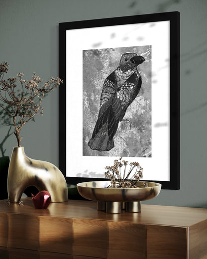 Black framed mixed media crow print on a dark teal wall above a wooden sideboard with brass vases of dried flowers and seed heads.