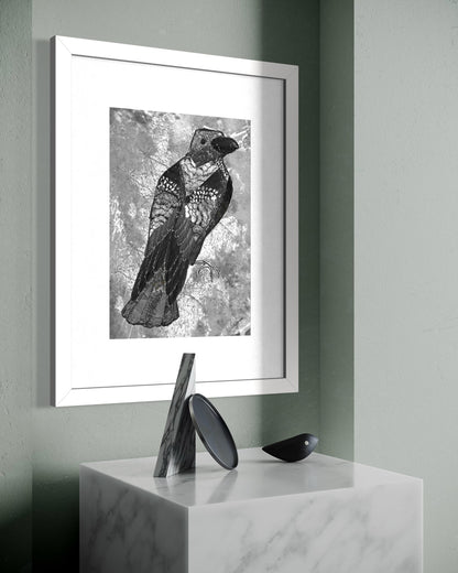 White framed crow art print on a sage green wall above a marble plinth holding a wooden curved form, a black disc and a small bird figurine.