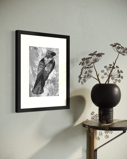 A4 black framed symbolic crow art print on a sage grey plaster wall, beside a round side table with a black vase of dried cow parsley.
