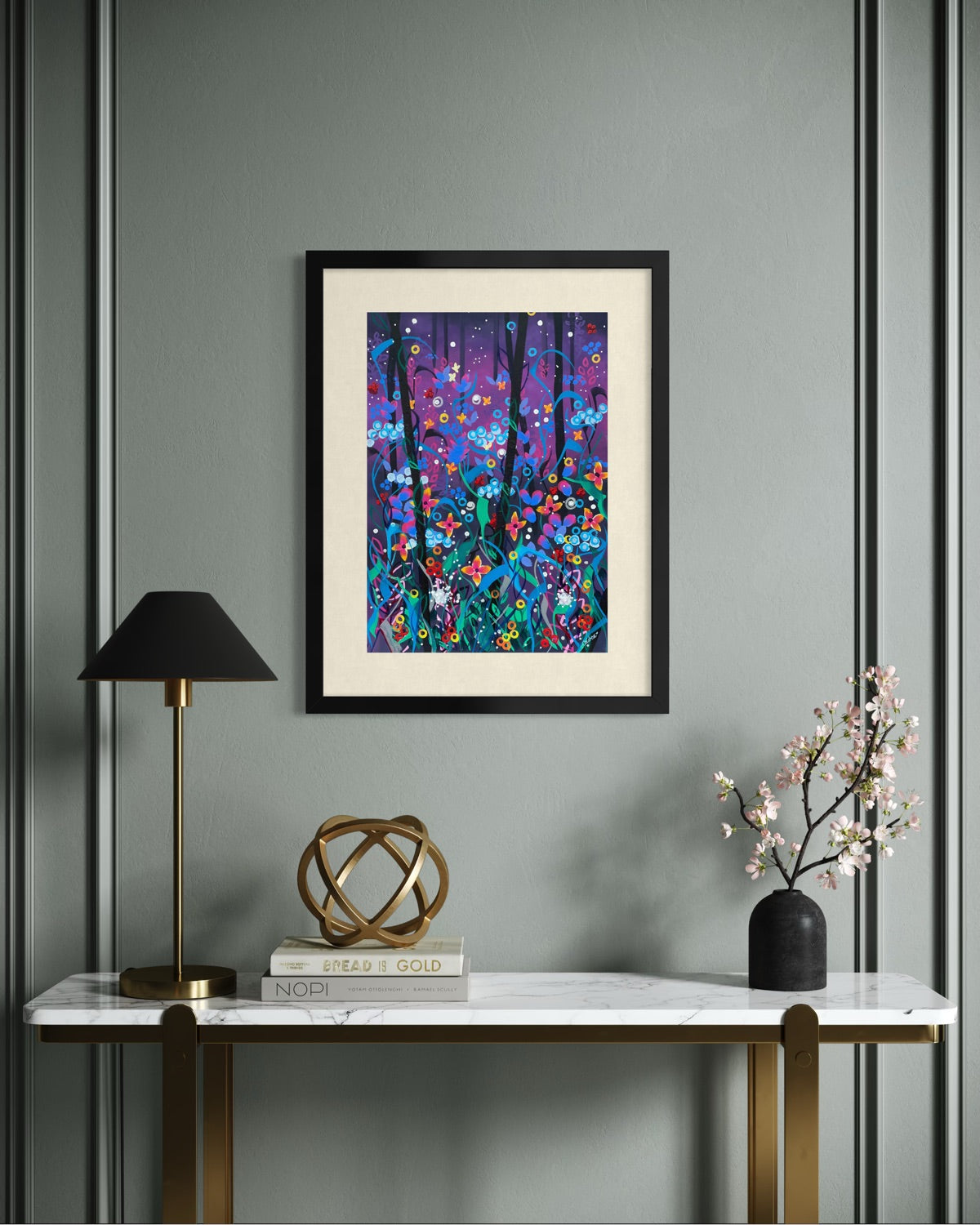 Black framed A2 wildflower art print on a sage panelled wall above a marble console with a brass lamp, cookbooks and cherry blossom.