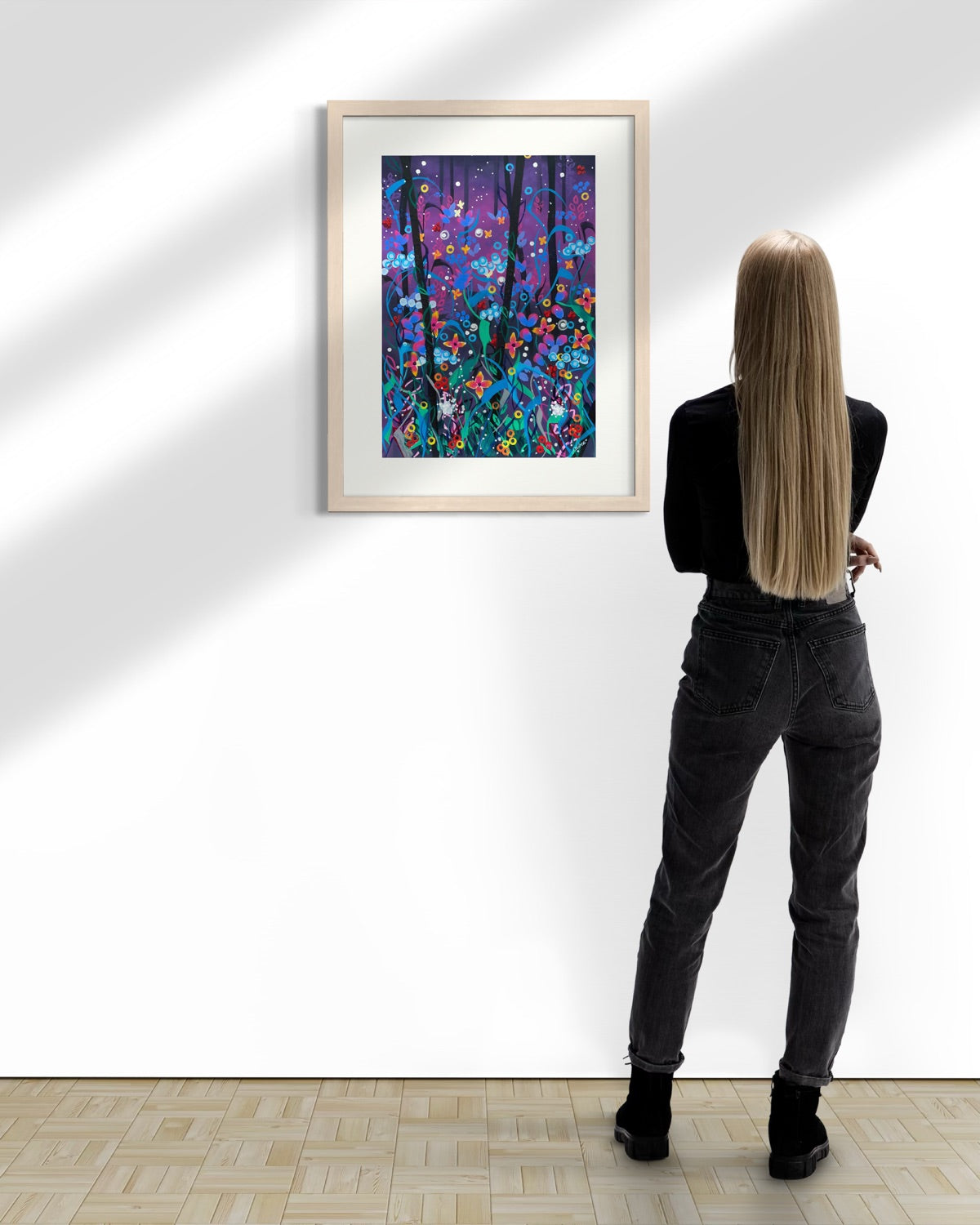 Natural wood A2 twilight floral painting on a sunlit white gallery wall above parquet flooring, viewed by a woman in black with blonde hair.