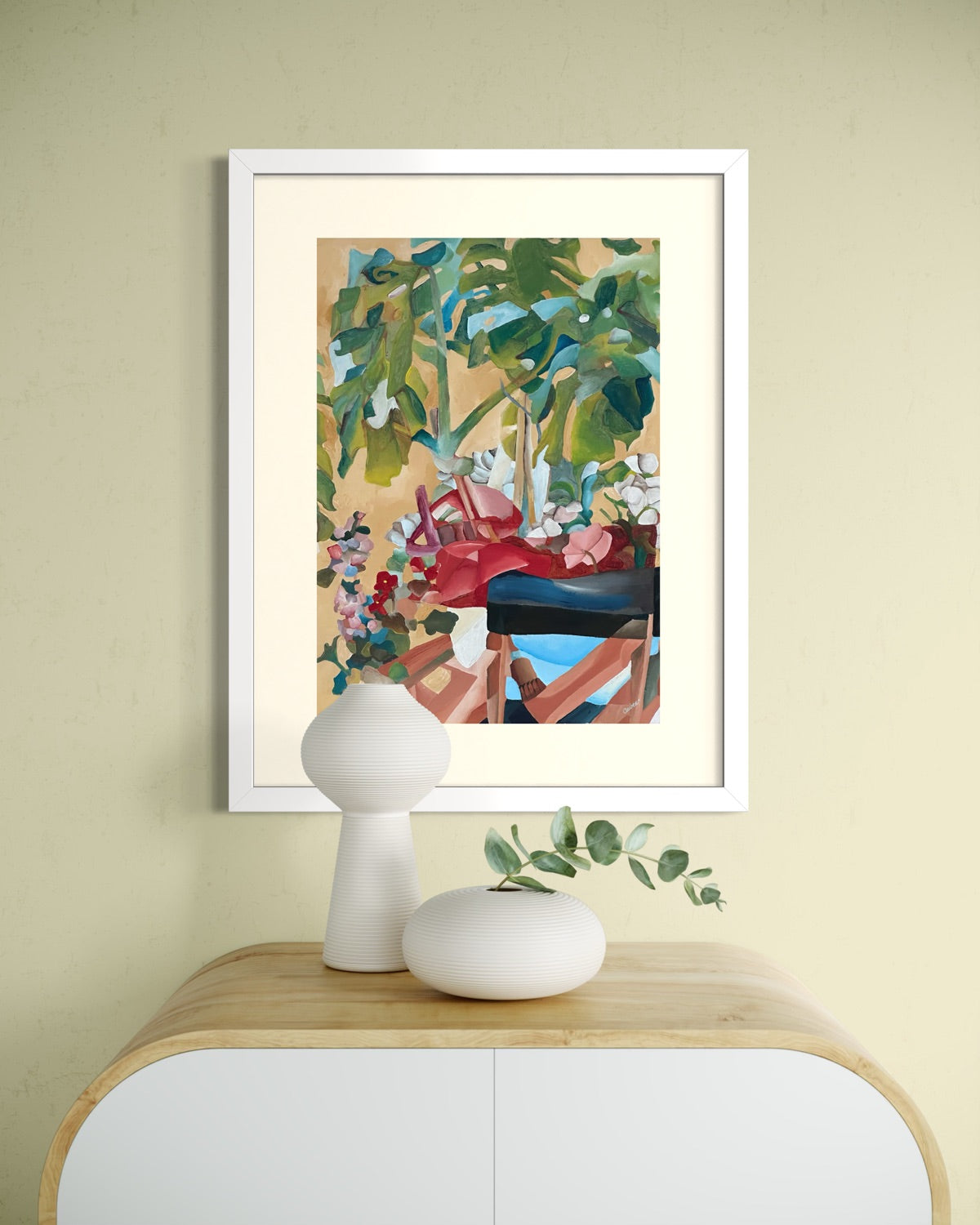 White framed A2 garden painting on a soft butter yellow wall above a curved oak sideboard with a ribbed gourd lamp and eucalyptus.